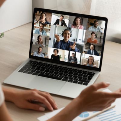 A person sits at a computer looking at the screen where a virtual meeting is taking place. The other people on the screen look engaged in the conversation