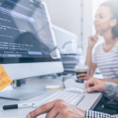 A person is working on a computer screen that is showing a lot of code. On the bottom of the monitor there is a sticky note reminding the person about a call