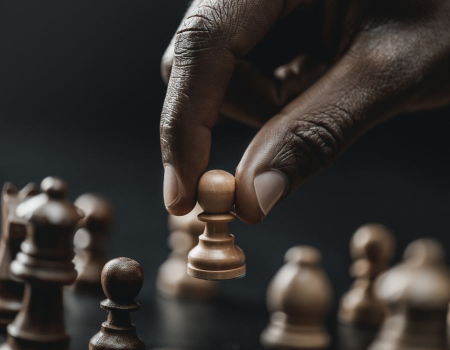 A person's hand holding a white pawn, moving it across a chessboard