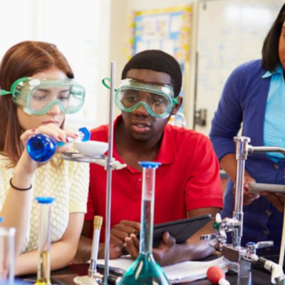 Two high school students working on a chemistry project together while their teacher watches.